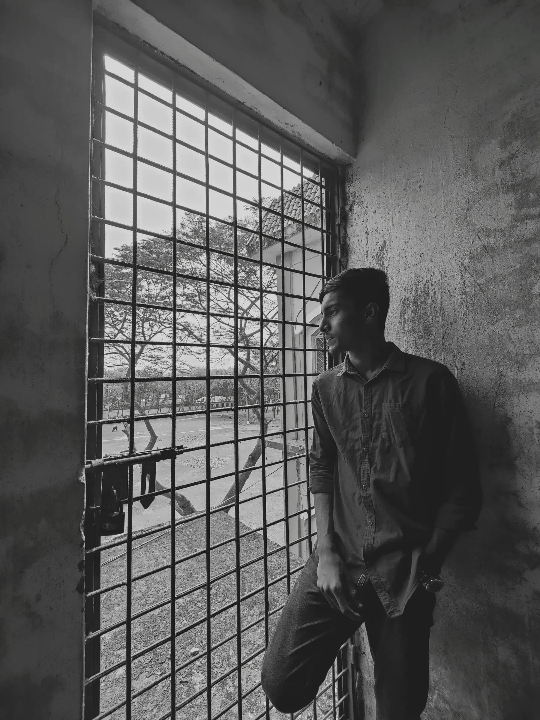 Profile portrait looking through an iron window grille against textured concrete wall