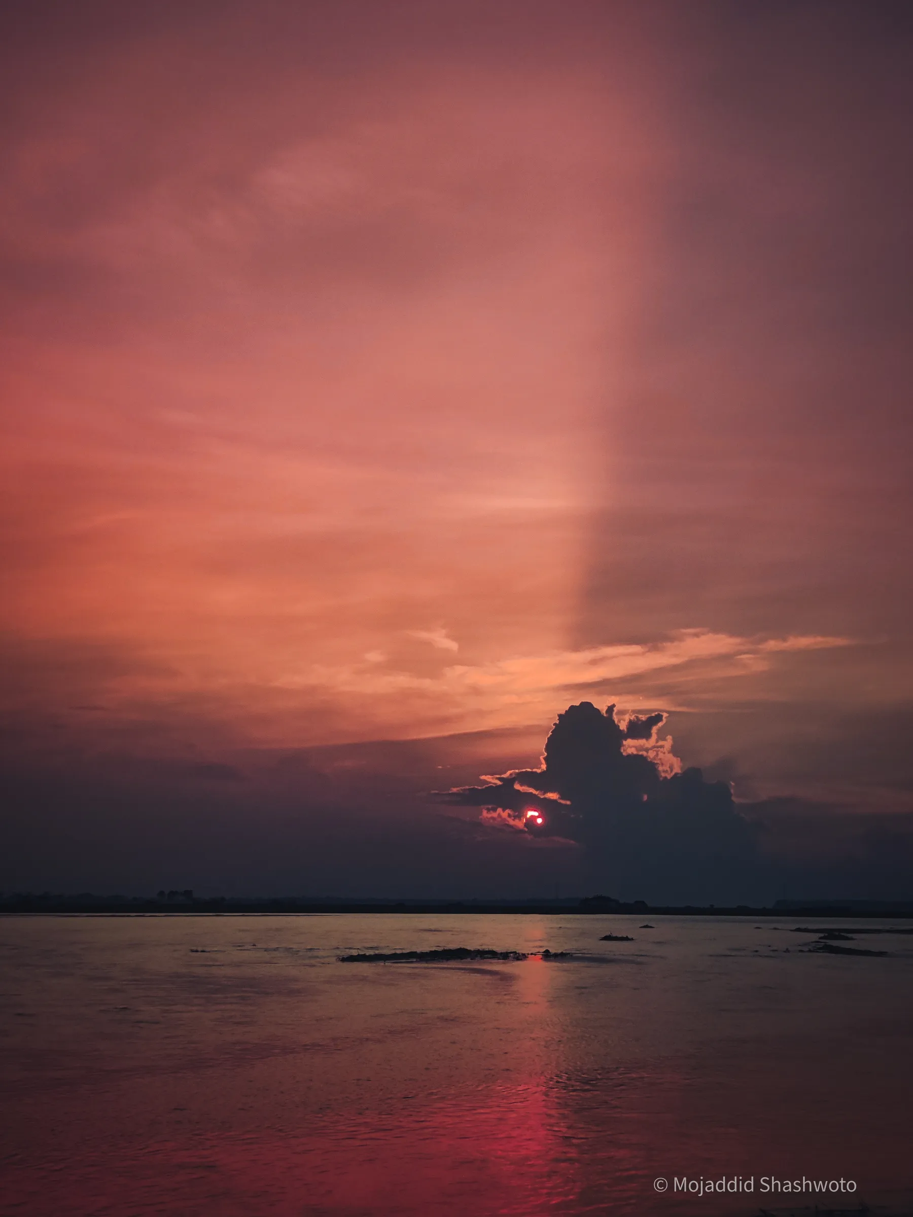 Vertical view of calm river and dark horizon under deep crimson sunset sky