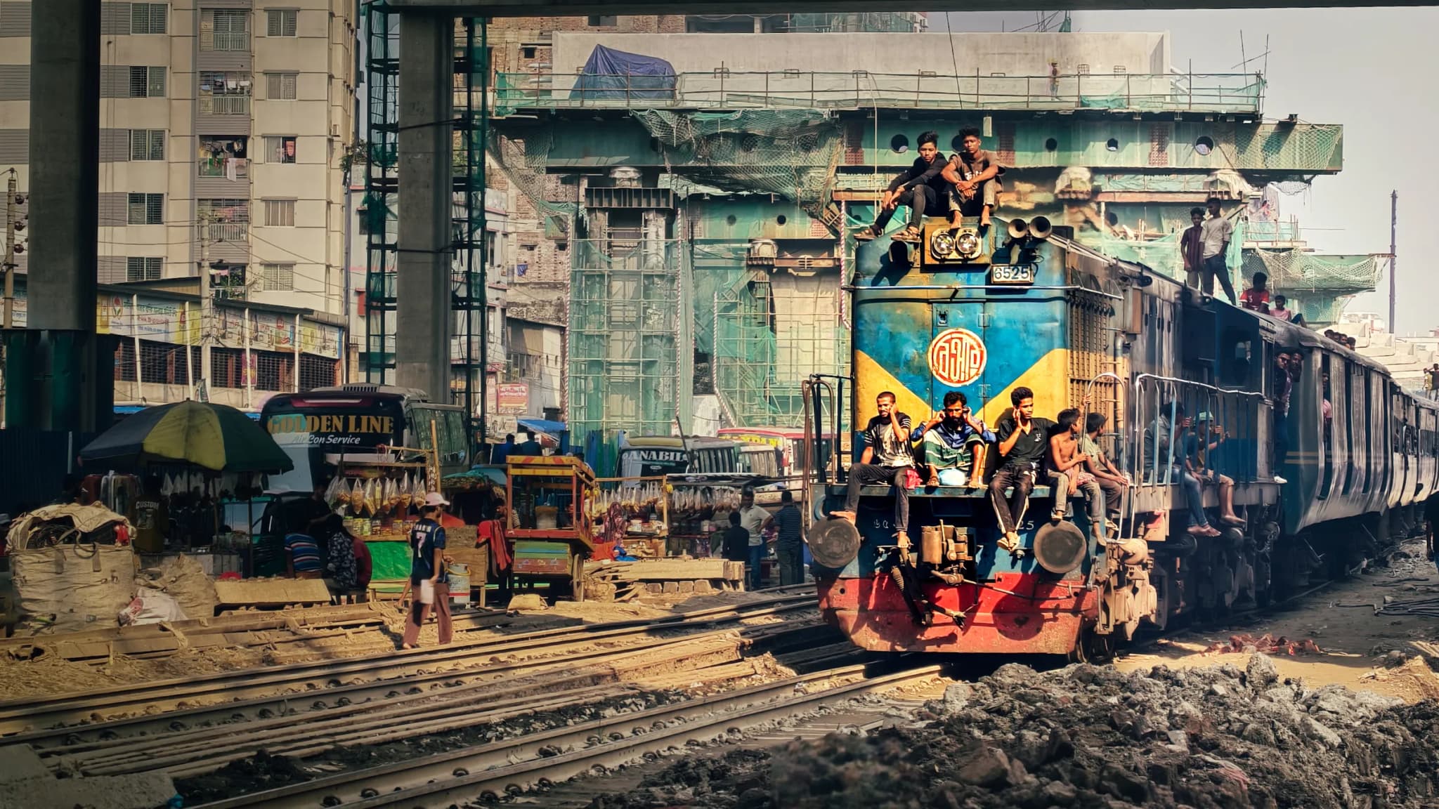 Wide perspective of railway tracks, bustling market stalls, and oncoming passenger train
