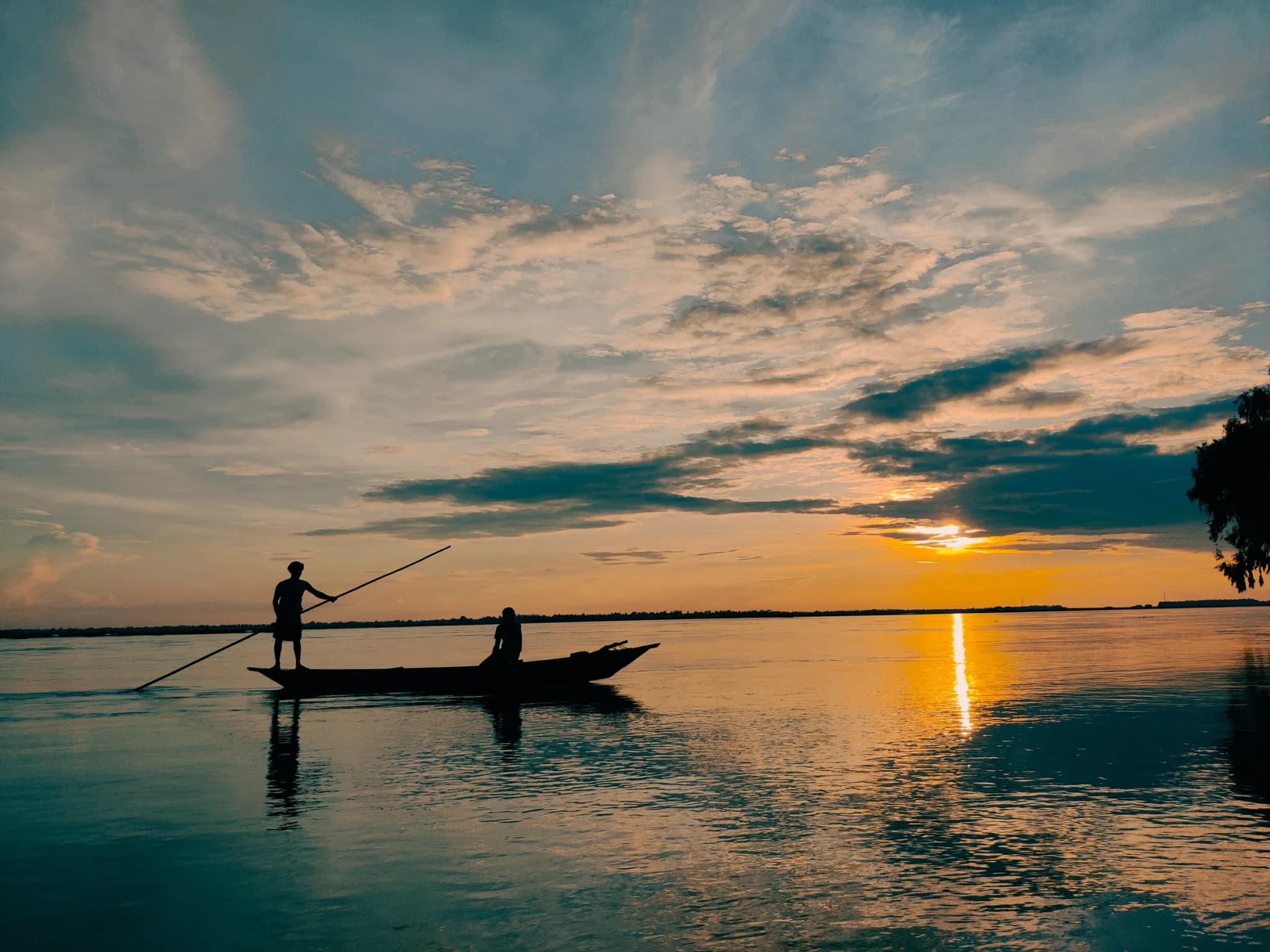 Silhouetted boatmen on a river under dramatic clouds and setting sun