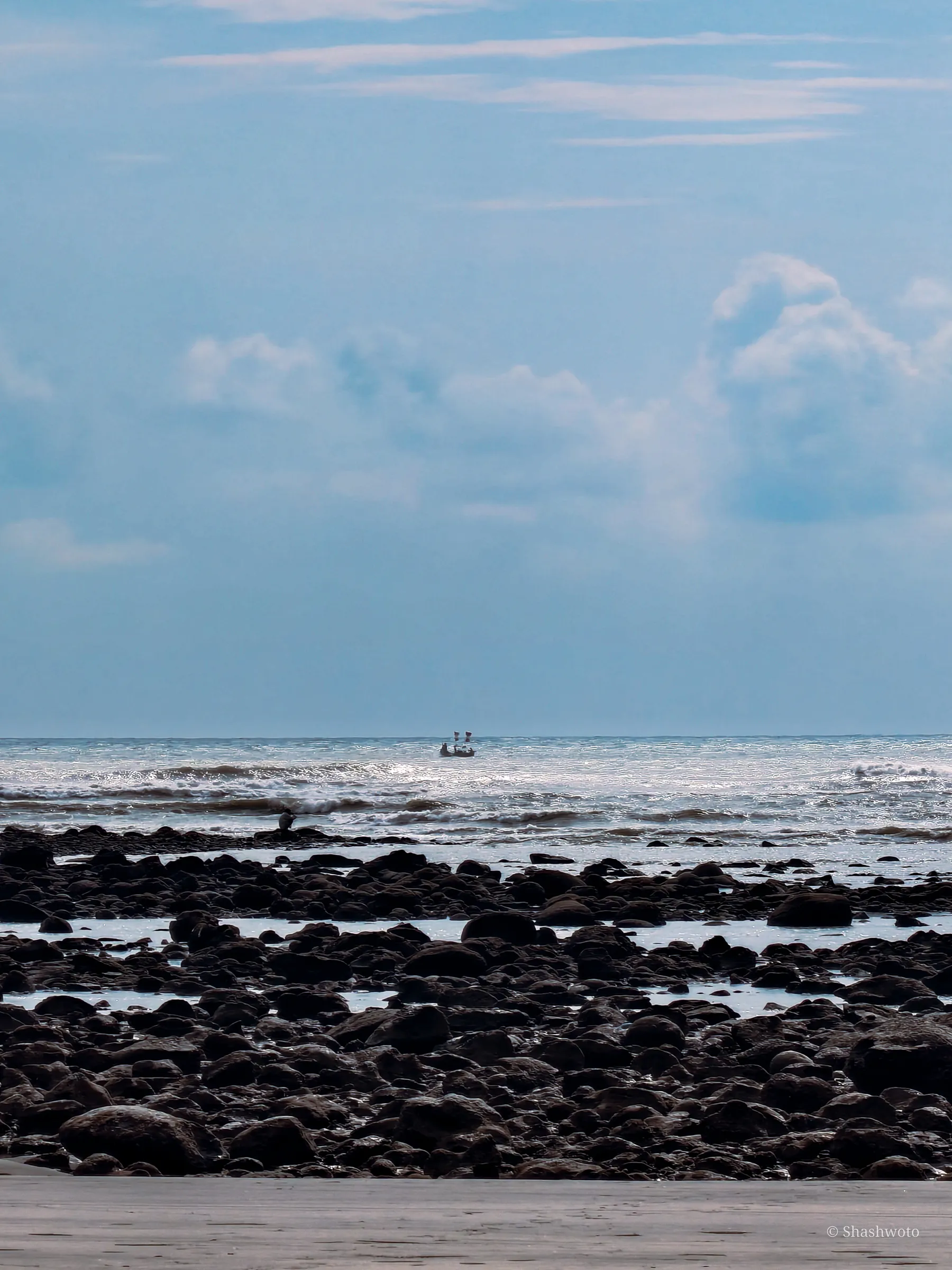 Rocky coastline with dark stones in the foreground and a solitary boat on the sea horizon