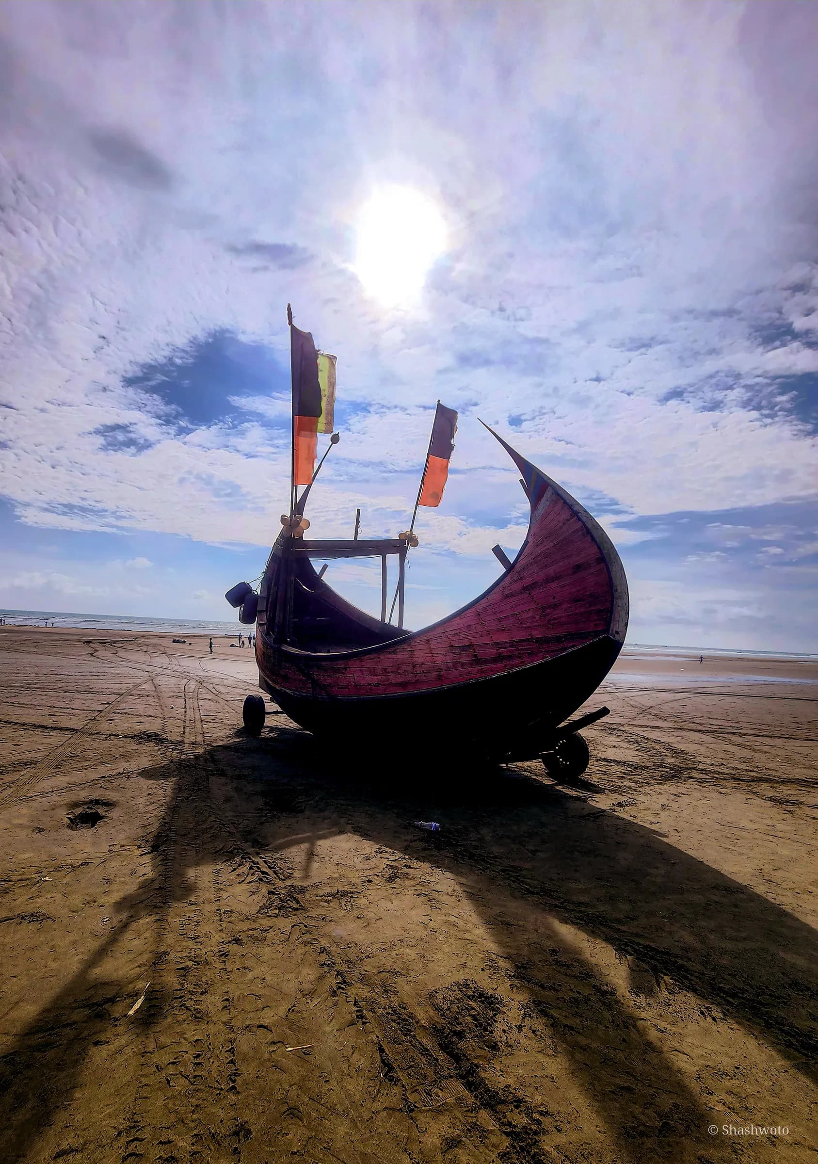 Crescent wooden fishing boat casting long shadow on beach sand under bright sun
