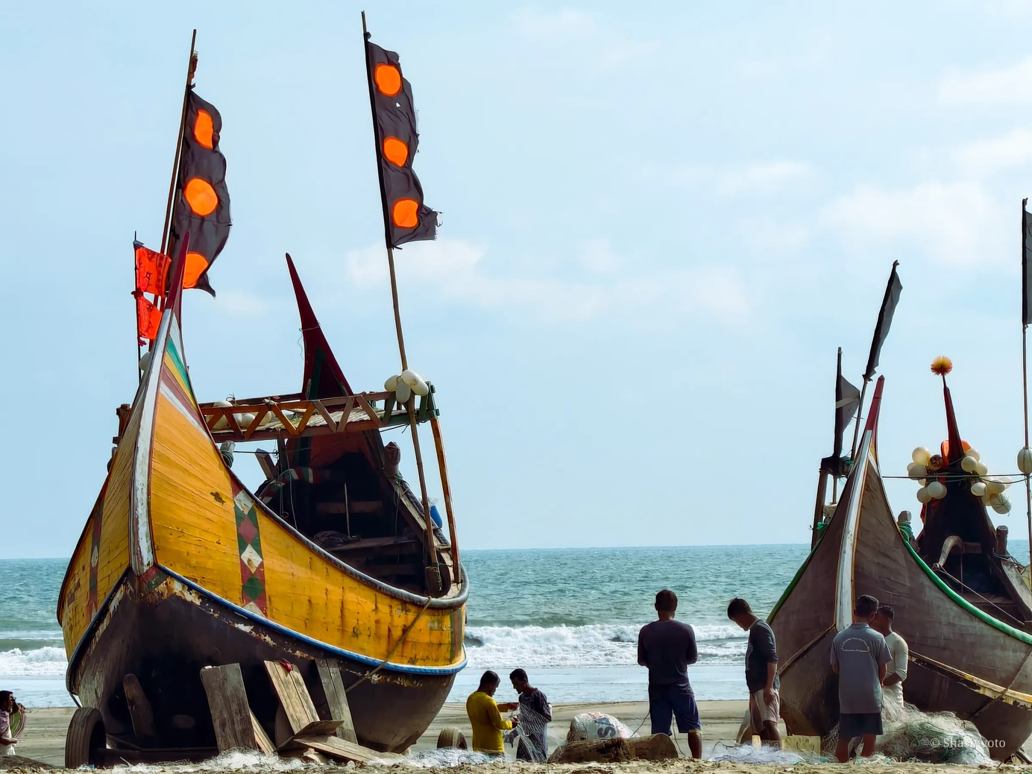 Yellow wooden moon boat with black flags on the sand with workers sorting nets